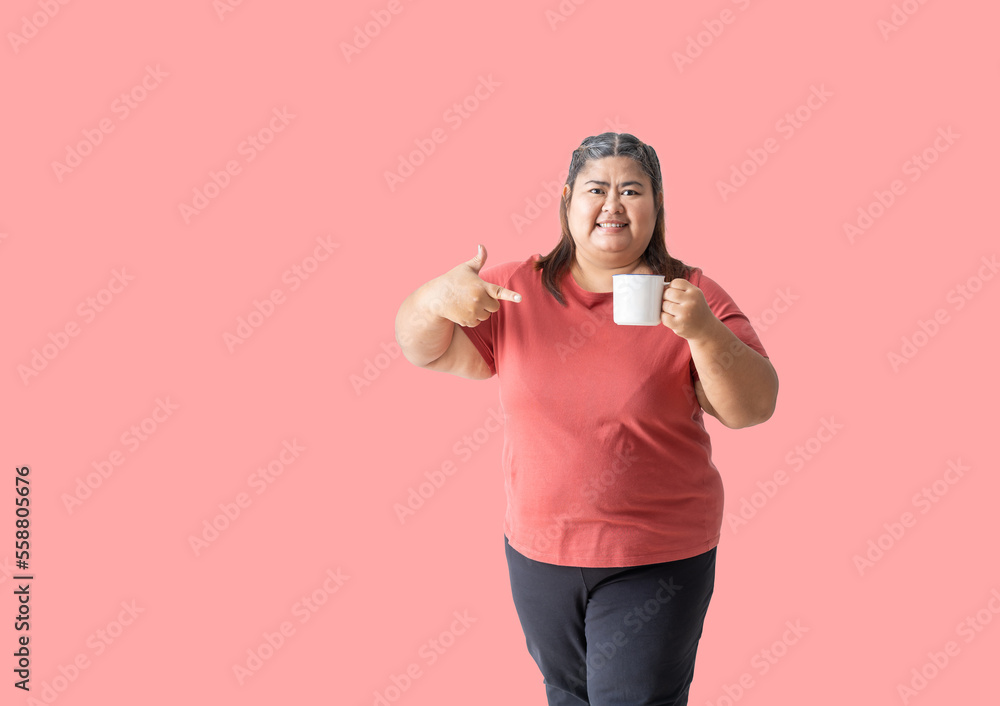 Fat woman asian happy smiling holding a mug with hand pointing, isolated on pink background Fat woman asian happy smiling holding a mug with hand pointing, isolated on pink background