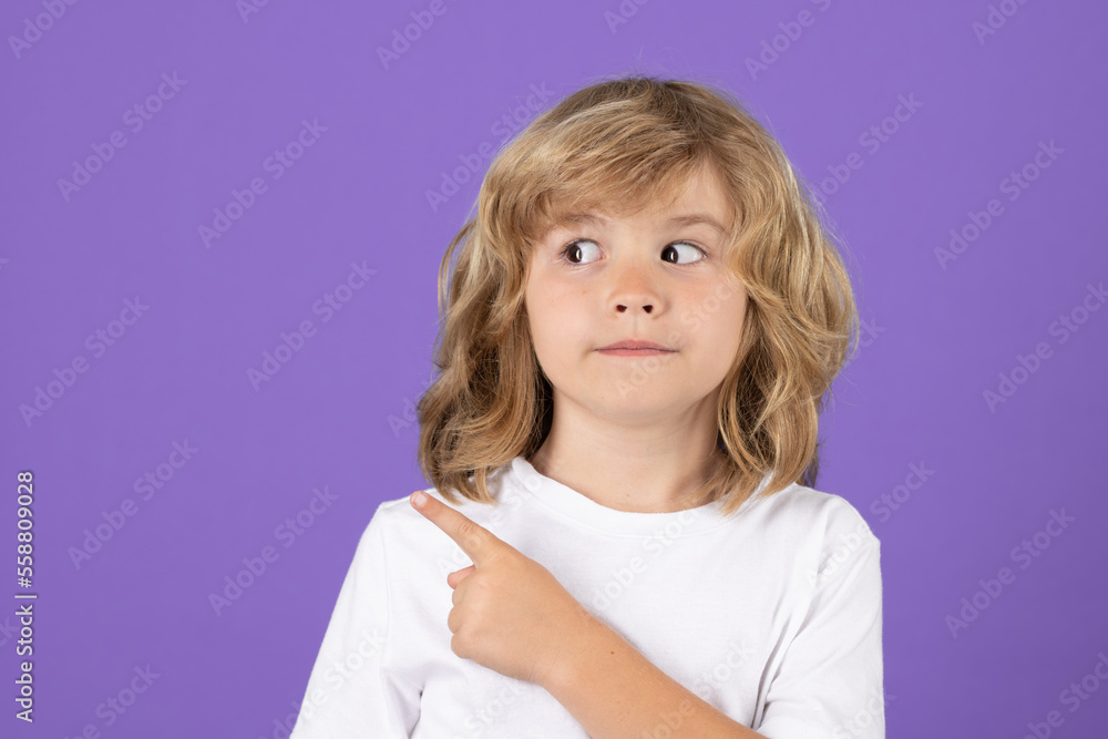Little child looking away, pointing finger on isolated studio background. Kid pointing to copyspace, showing promo offers, points away. Advertisement promo product concept.