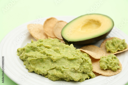 Delicious guacamole, avocado and chips on light green background, closeup