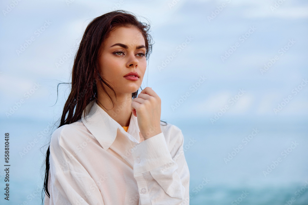 Portrait of a beautiful pensive woman with tanned skin in a white beach shirt with wet hair after swimming on the ocean beach sunset light with clouds, the concept of freedom and mental health Portrait of a beautiful pensive woman with tanned skin in a white beach shirt with wet hair after swimming on the ocean beach sunset light with clouds, the concept of freedom and mental health