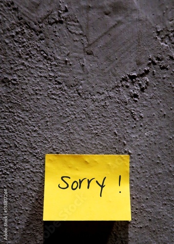 Grey rough textured wall with yellow notepad/post-it written SORRY,concept of making apology to someone