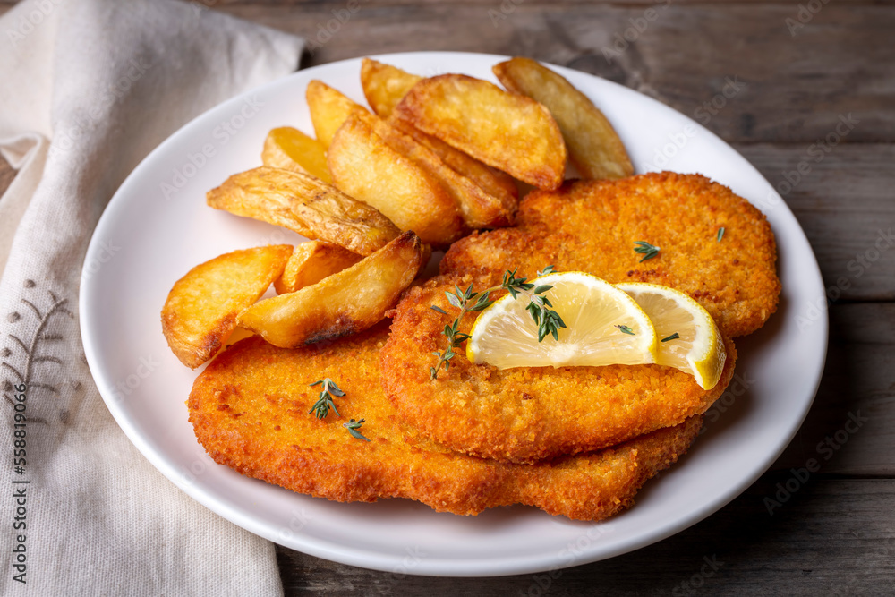 Chicken schnitzel with sauce, fried potatoes and lemon in a plate Chicken schnitzel with sauce, fried potatoes and lemon in a plate
