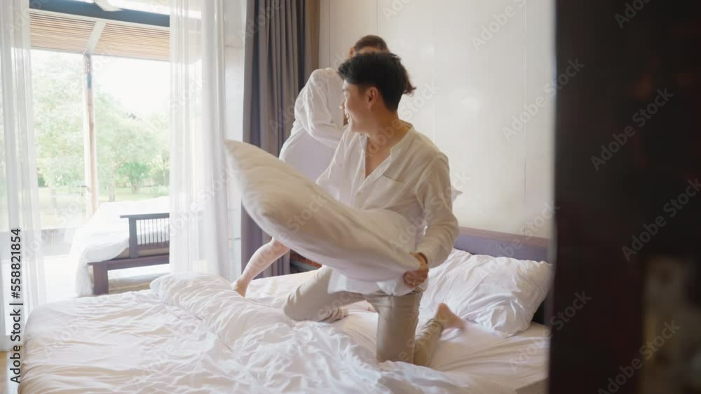 Young adult couple two asia people relax joy fun smile laugh spend good time play pillow fight war on bed at cozy home asian lover just married man woman in family day life begin happy sweet moment.