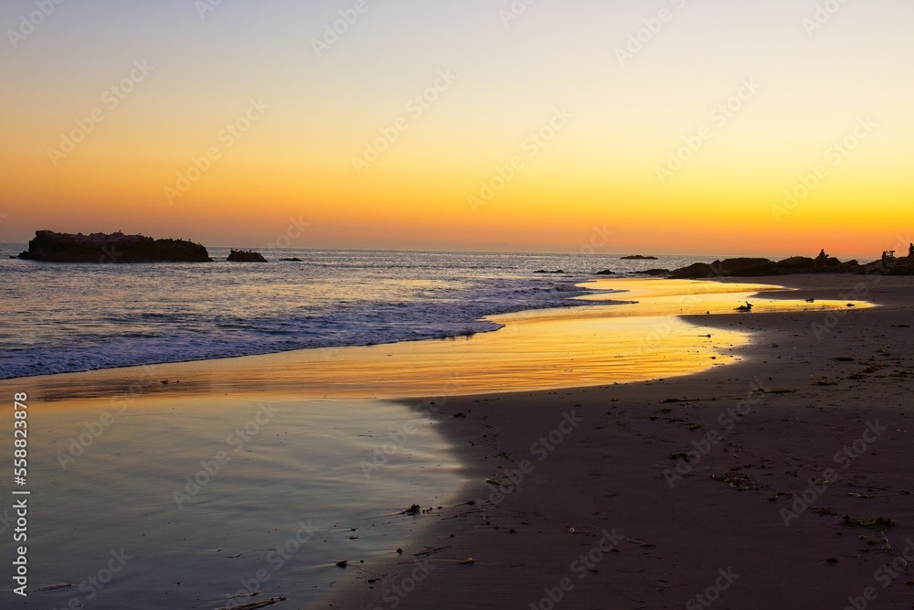 A golden sunset at the beach with the sunset reflecting off of water on the sand. Laguna Beach, California.