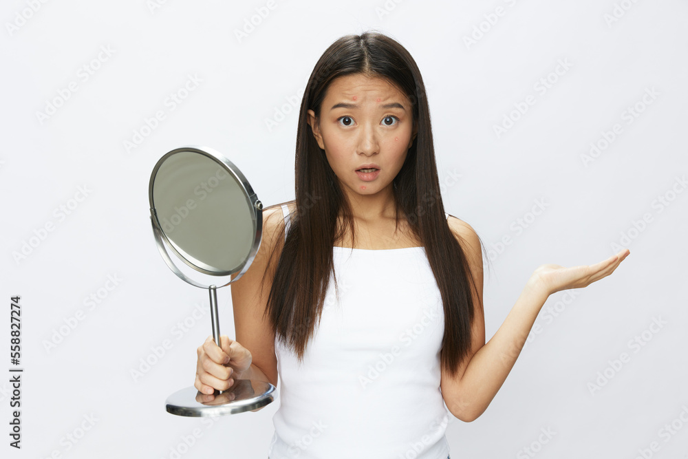 Asian woman with mirror in hand facial skin problems, acne and inflammation, red rash and allergies, chicken pox, sadness from rashes. Facial skin care concept for diseases and nerves Asian woman with mirror in hand facial skin problems, acne and inflammation, red rash and allergies, chicken pox, sadness from rashes. Facial skin care concept for diseases and nerves