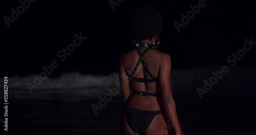 Sexy bikini babe on the beach at night spins in her outfit with waves in the background photo