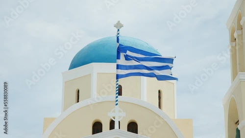 Greek flag waving in front of Saint George Church dome, Oia village, Santorini, Greece photo