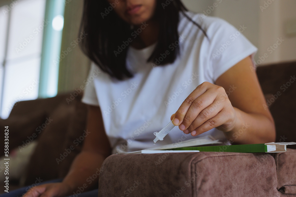 Asian woman using rapid antigen test kit for self testing COVID-19 at home. Close up woman hand dropping sample fluid on test kit. Asian woman using rapid antigen test kit for self testing COVID-19 at home. Close up woman hand dropping sample fluid on test kit.