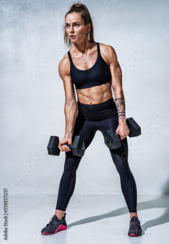 Sporty woman resting after workout with dumbbells. Photo of woman with good physique on grey background. Strength and motivation. Full length