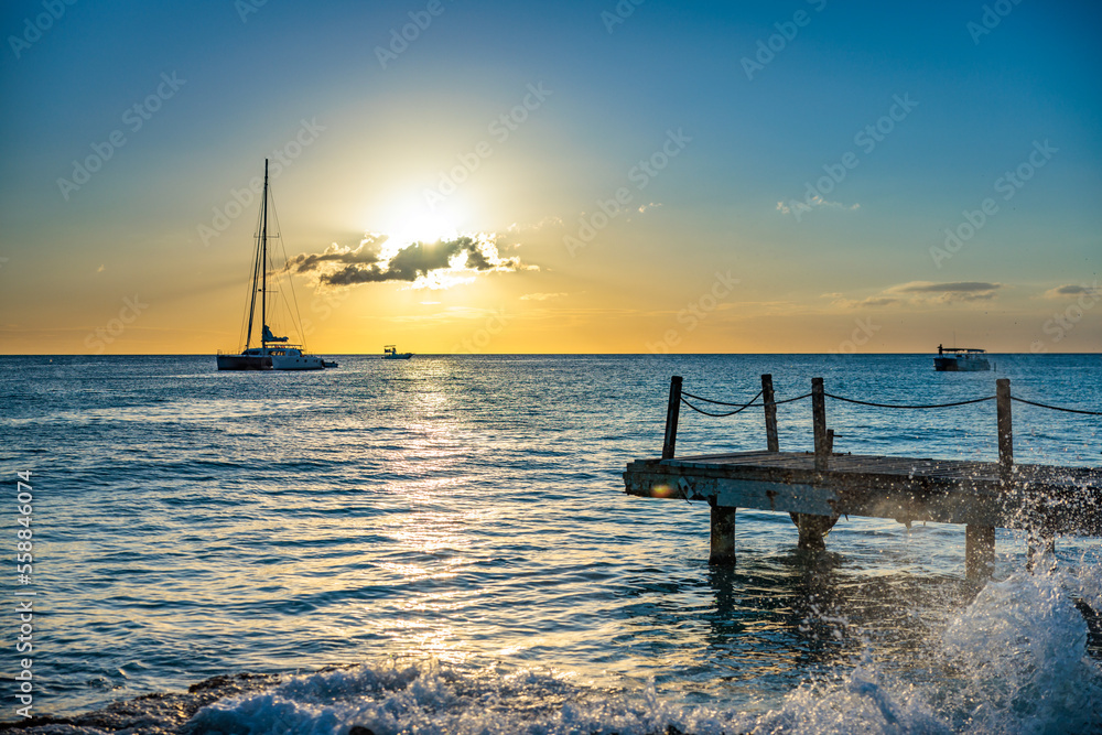 Sunset on the Caribbean Sea, with a pier in the foreground and a sailboat in the background, Bayahibe, Dominican Republic