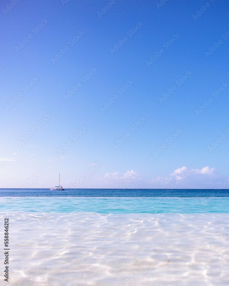 Fototapeta premium Sailing boat at the horizon , between infinity pool , sea and sky, Punta Cana, Dominican Republic