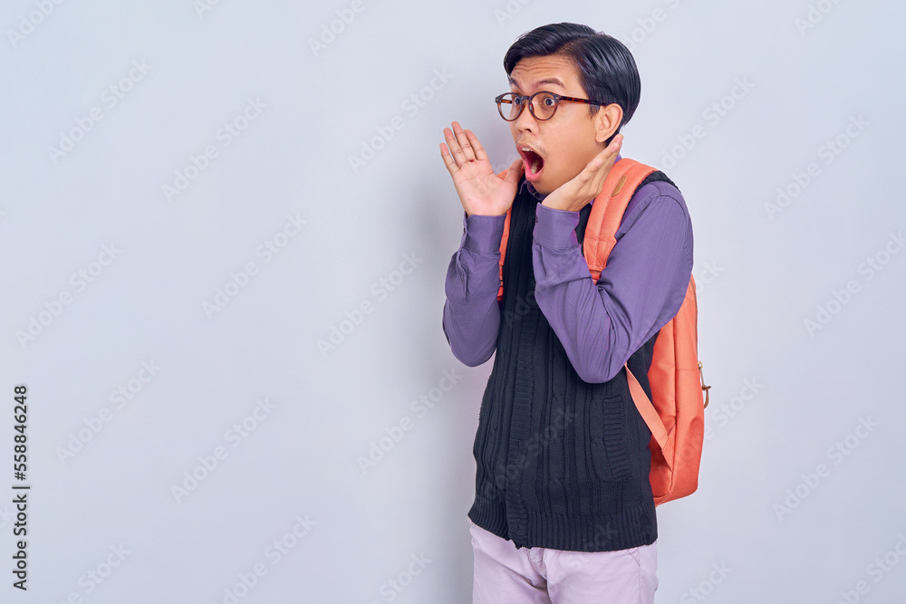 Surprised young Asian student man in casual clothes with backpack looking away with open mouth isolated on gray background. High school university college concept Surprised young Asian student man in casual clothes with backpack looking away with open mouth isolated on gray background. High school university college concept