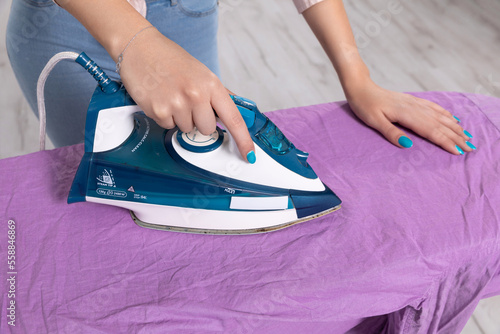 A woman's hand holds an iron and irons a man's shirt on the ironing board.