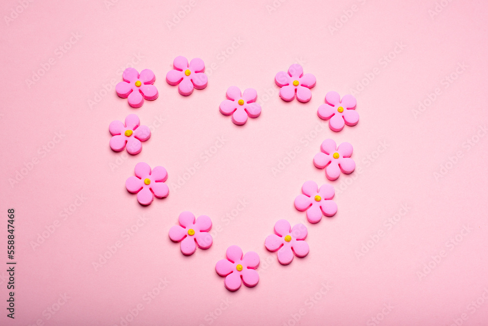 Heart-shaped frame made with sugar flowers on a pink background. Concept of love