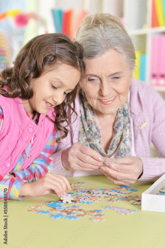 Fototapeta premium Grandmother with granddaughter collecting puzzle at home