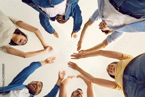 Satisfied group of cheerful friends cheering, celebrating good result and goal achievement. Joyful young people in casual clothes laughing celebrating success raising hands together. View from below.