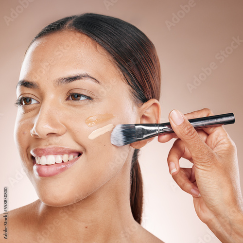 Beauty, makeup and woman with foundation in a studio for cosmetic skincare routine with a brush. Cosmetics, skin and happy girl model from Mexico with a luxury face tone isolated by brown background. photo