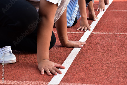 Group of young southeast asian boys put their hands on white line on running track to run during their school outdoor freetimes activity, spending freetimes, and lifestyle of raising teens concept.