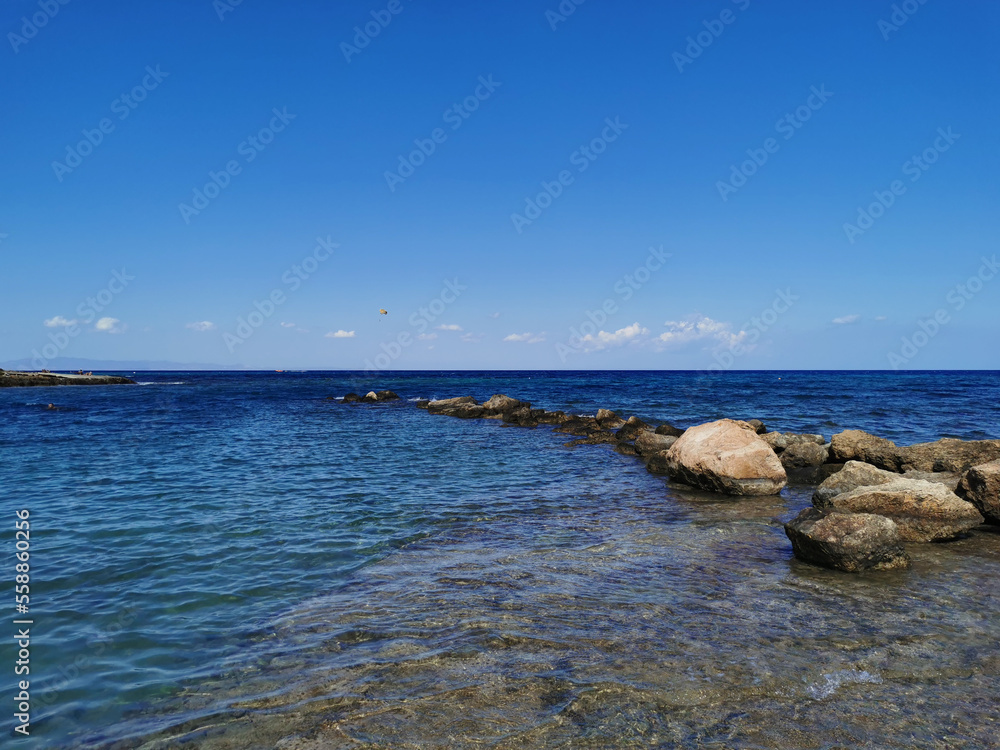 The coast of the Mediterranean Sea, waves, clear water, a stone ridge against a blue sky with clouds. The coast of the Mediterranean Sea, waves, clear water, a stone ridge against a blue sky with clouds.