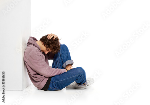 Portrait of young boy sitting on floor in depression and sadness over white background. Problems of youth © master1305