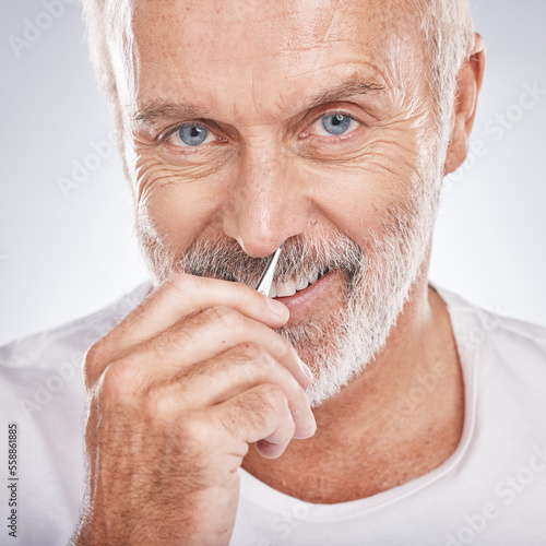 Portrait, tweezers and nose with a senior man in studio on a gray background for grooming or personal hygiene. Face, hand and equioment with a mature male tweezing to remove nasal hair in a bathroom photo