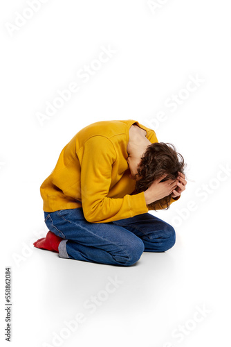 Portrait of young boy sitting on floor and suffering from mental breakdown over white background. Emotional stress, depressive condition © master1305
