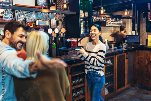 Young female waitress or bartender serving drinks in a bar carrying a tray with beer