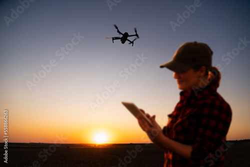 Farmer controls drone sprayer with a tablet on a sunset. Smart farming and precision agriculture 