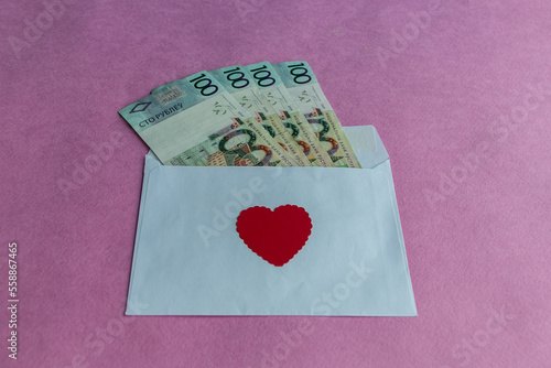 Hundred-ruble Belarusian banknotes in a paper envelope with a red heart on a pink background. Conceptual gift for Valentine's Day, wedding, birthday.