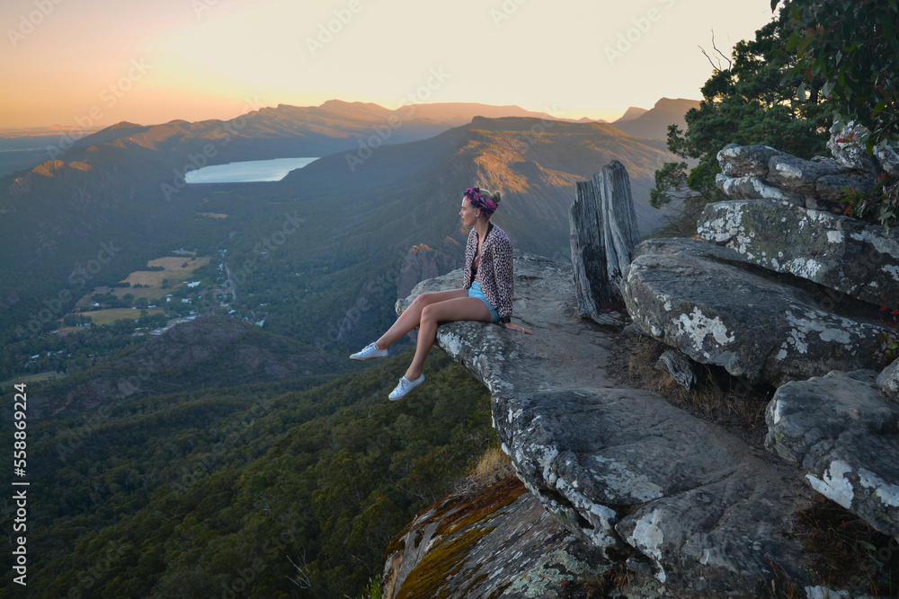 Woman sitting on rock dangling feet off mountain top