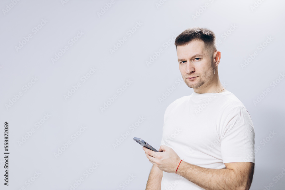 A man in a white T-shirt holds a mobile phone in his hand. Attractive guy A man in a white T-shirt holds a mobile phone in his hand. Attractive guy