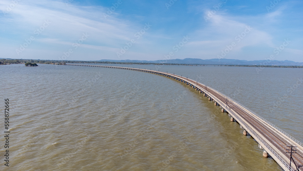 Aerial view of an amazing travel train parked on a floating railway bridge over the water of the lake in Pa Sak Jolasid dam with blue sky at Lopburi, Thailand.