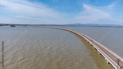 Aerial view of an amazing travel train parked on a floating railway bridge over the water of the lake in Pa Sak Jolasid dam with blue sky at Lopburi  Thailand.