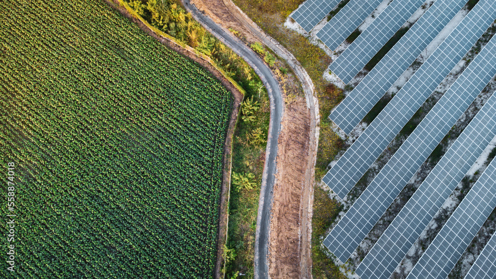 Fly over Solar cells farm beside nature green farm around large industrial factory area. Solar farms are generating renewable energy for the industry.