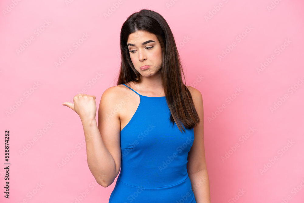 Young Brazilian woman isolated on pink background unhappy and pointing to the side Young Brazilian woman isolated on pink background unhappy and pointing to the side