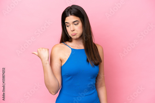 Fototapeta Naklejka Na Ścianę i Meble -  Young Brazilian woman isolated on pink background unhappy and pointing to the side