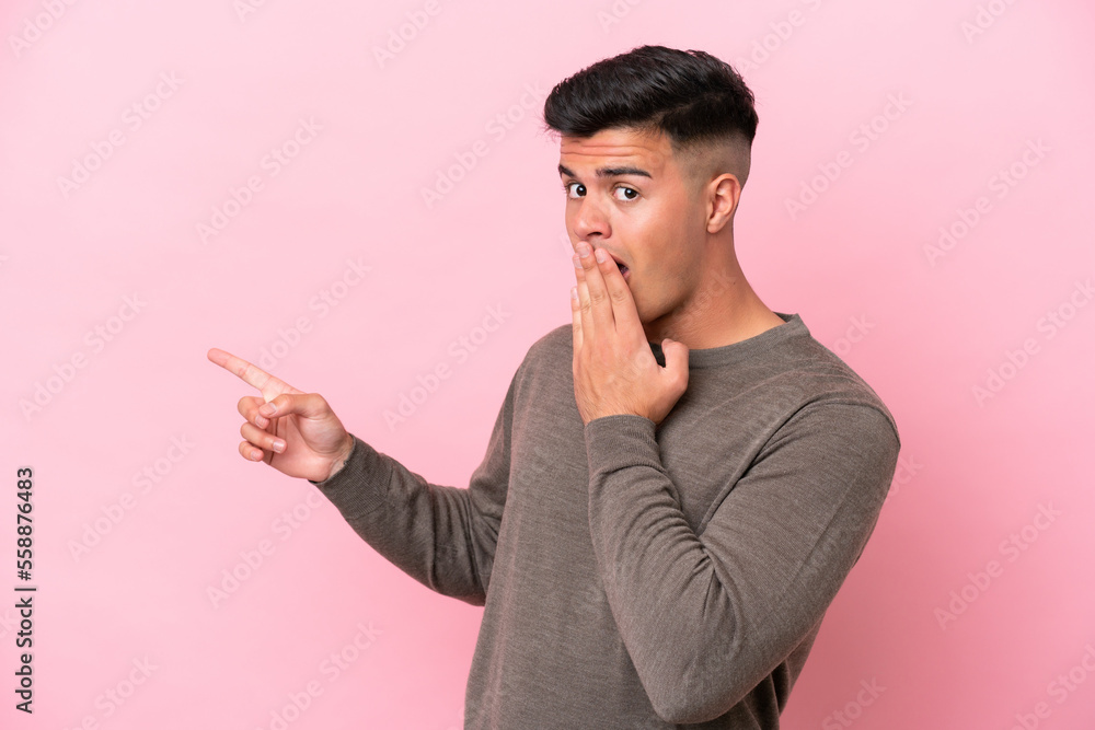 Young caucasian handsome man isolated on pink background with surprise expression while pointing side Young caucasian handsome man isolated on pink background with surprise expression while pointing side