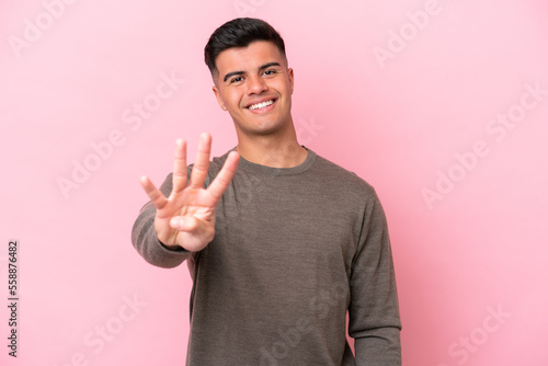 Young caucasian handsome man isolated on pink background happy and counting four with fingers