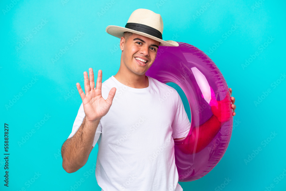 Young caucasian man holding air mattress isolated on blue background saluting with hand with happy expression Young caucasian man holding air mattress isolated on blue background saluting with hand with happy expression