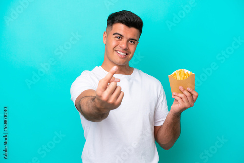 Young caucasian man catching french fries isolated on blue background doing coming gesture © luismolinero