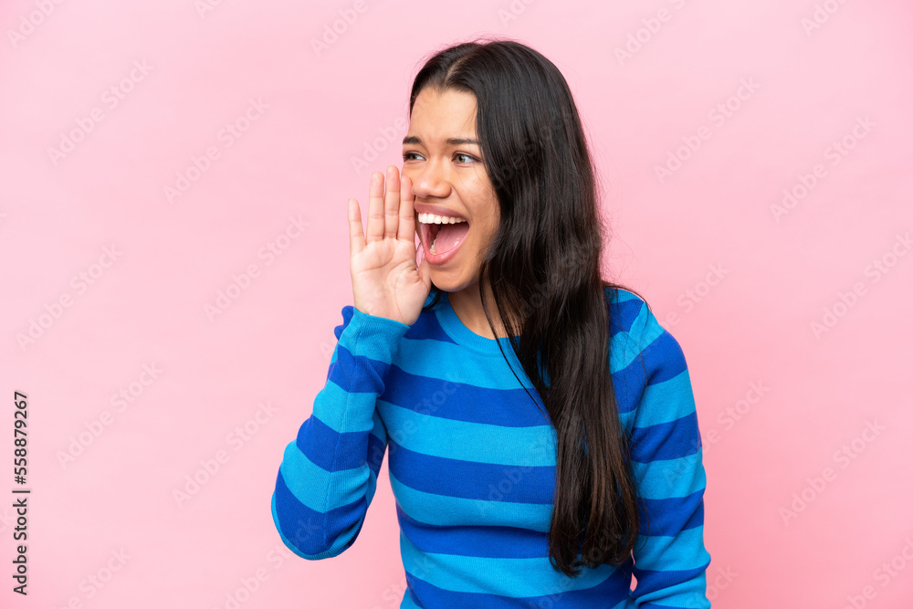 Young Colombian woman isolated on pink background shouting with mouth wide open to the side Young Colombian woman isolated on pink background shouting with mouth wide open to the side