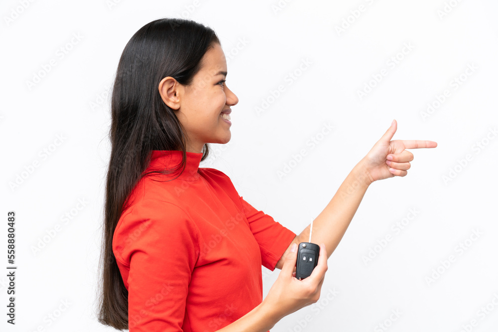Young Colombian woman holding car keys isolated on white background pointing to the side to present a product Young Colombian woman holding car keys isolated on white background pointing to the side to present a product