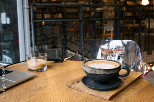 Cozy remote working morning in cafe - cup of delicious cappuccino coffee, laptop on desk and books