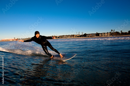 A male surfer wearing a hood leans into a bottom turn while surfing at Port Hueneme Beach in the city if Port Hueneme, California. photo