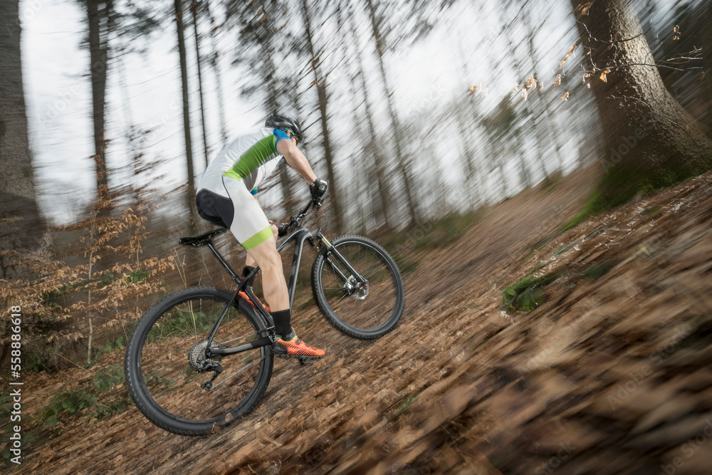 Side view of biker riding in speed through forest Side view of biker riding in speed through forest