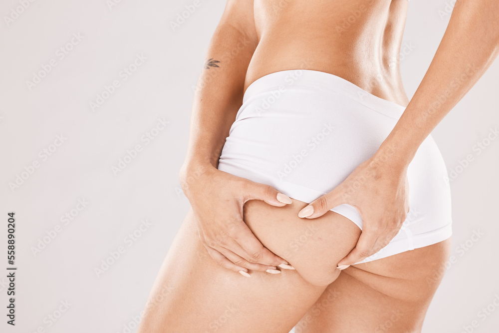 Hands, butt and underwear with a woman model in studio on a gray background squeezing cellulite from the back. Liposuction, wellness and heath with a female touching her buttocks or ass in panties