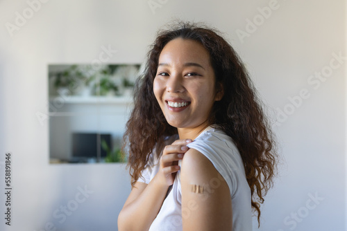 Young Asian woman with adhesive bandage on her arm after Corona virus vaccine. First aid. Medical, pharmacy and healthcare concept.