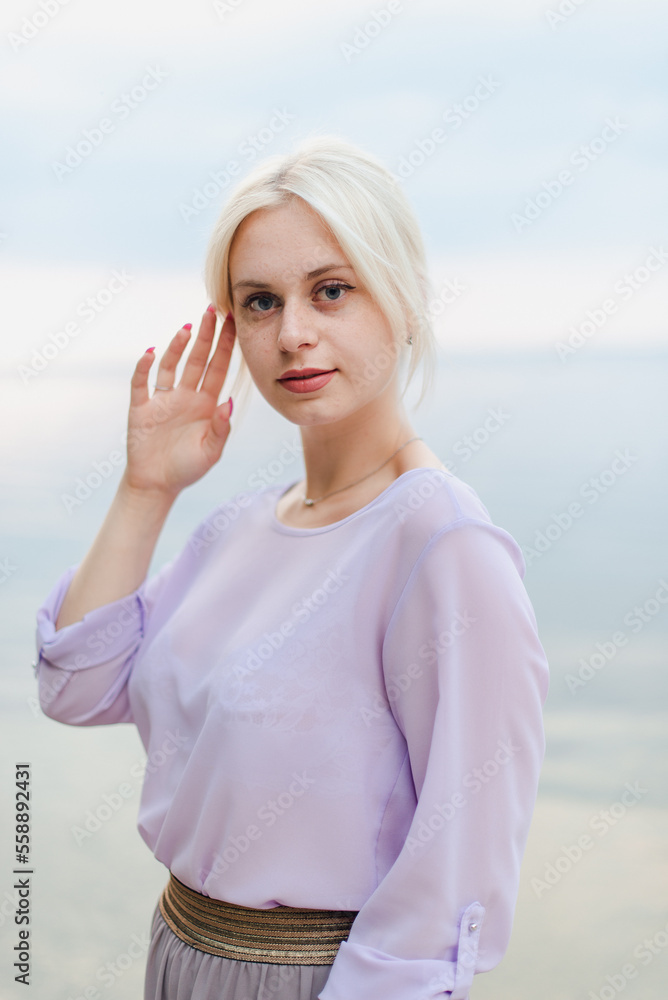 Blonde girl on a summer day on the shore near the river in nature in a dress