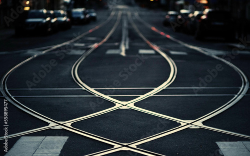 Photo of crossed white steel railroad tracks on the road paved with black asphalt with black background and has a car in the background