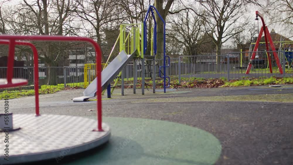 Panning shot of an empty children's playground as a roundabout comes to a slow stop